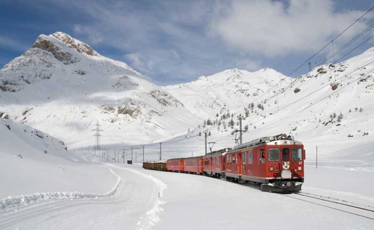 Nell' immagine si mostra il paesaggio innevato della Valtellina. Tra la valle innevata passa il trenino rosso del Bernina.
