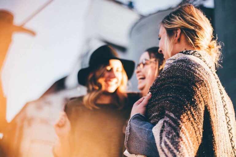 In the image there are three girls smiling and hugging each other.