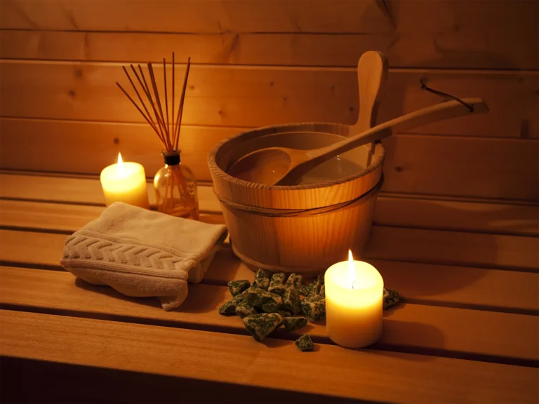 Pictured is a small wooden table with spa essentials on it: a towel, two scented candles, stones, spa water, and fragrance diffuser.